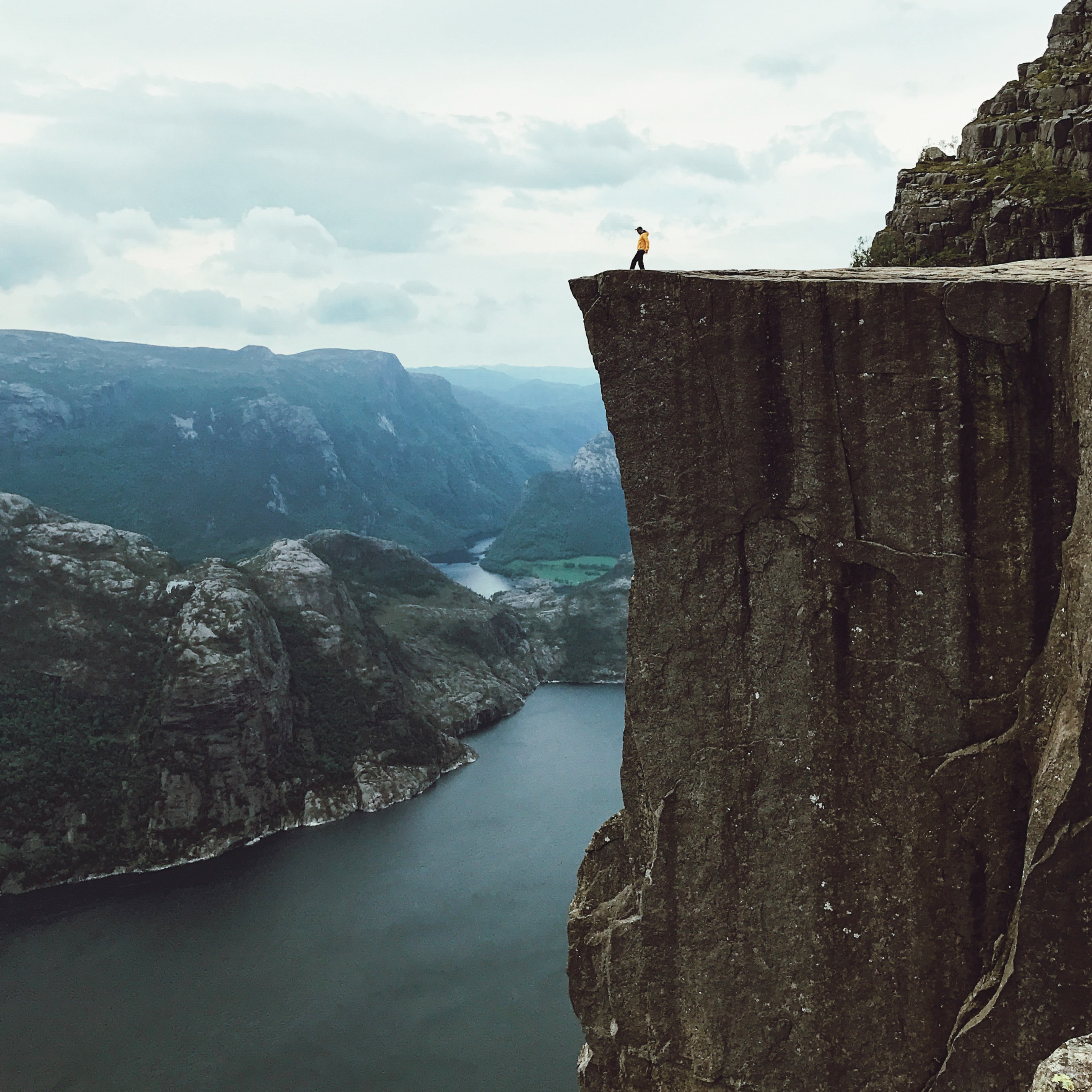 Man with a yellow jacket poses on the top of the rock